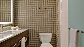 Un baño con pared de estampado pata de perro, inodoro blanco, lavamanos con espejo y perchero para toallas.