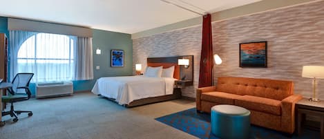 A hotel room with a bed, a sofa, a desk, and a chair.