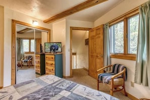 Une chambre  à coucher avec un lit, une commode, une chaise, un miroir et une fenêtre avec des rideaux.