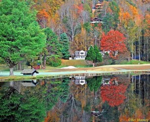A house with a pond in front, surrounded by trees with autumn foliage.