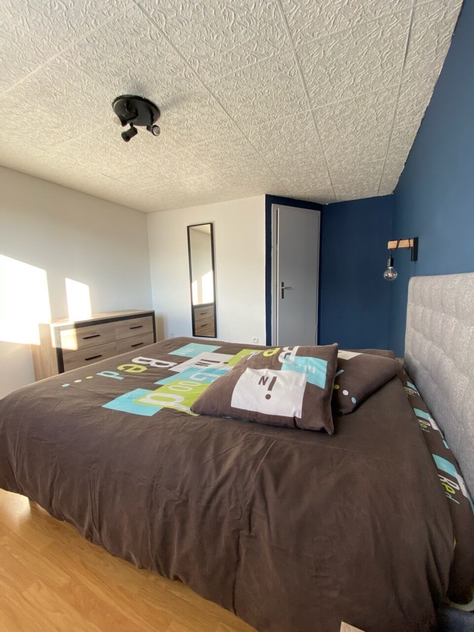 Ein Schlafzimmer mit Bett, Kommode, Spiegel und Tür.