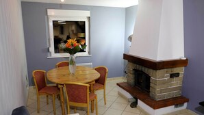 A dining area with a round wooden table and four chairs, a vase with flowers, and a stone fireplace. - Maison Rurale En Bordure De Forêt (Schirmeck)