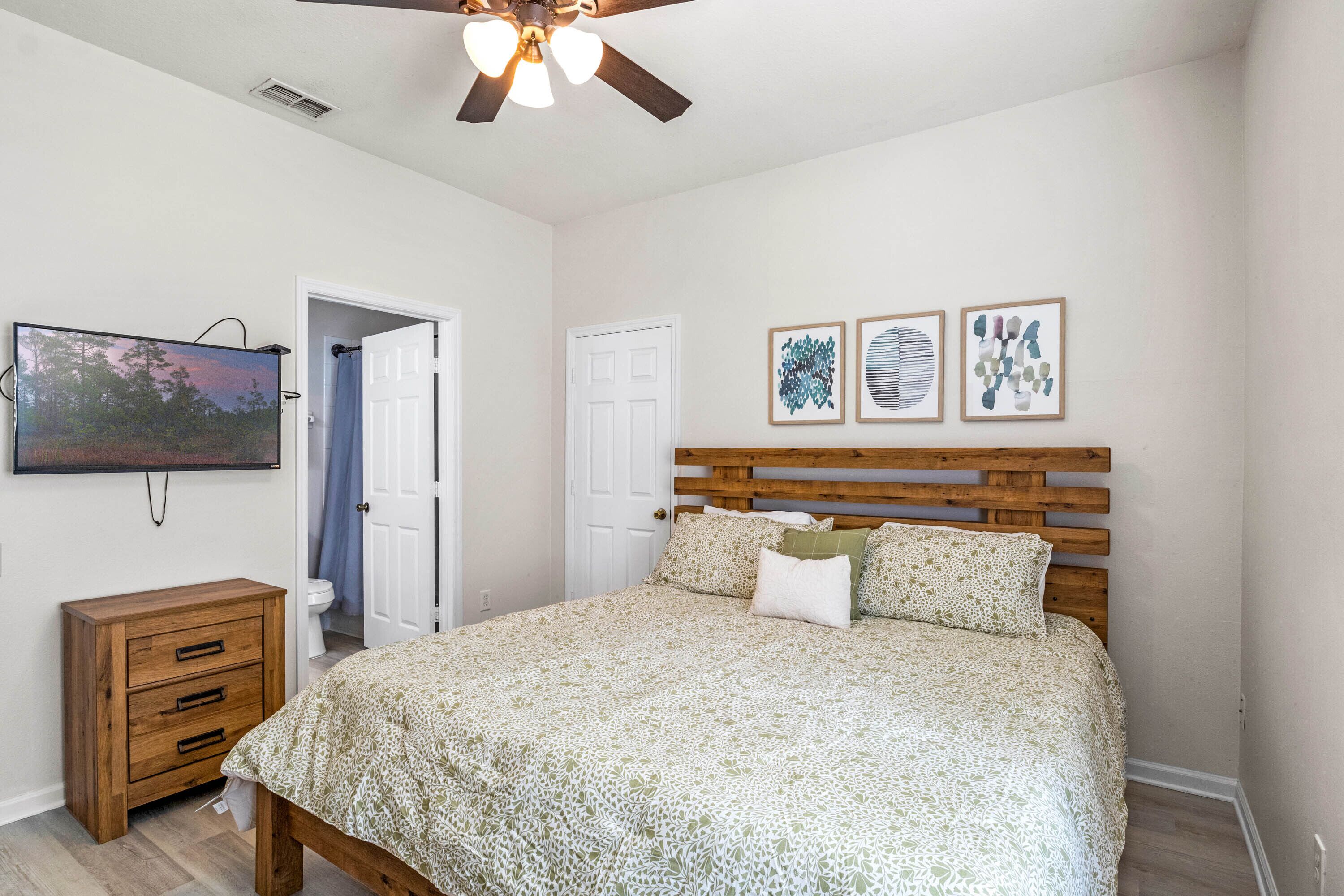 A bedroom with a wooden bed, a nightstand, a ceiling fan, and wall art.