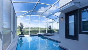 Une piscine extérieure moderne, dotée d’une structure en verre, entourée d’un bâtiment blanc avec une porte et des fenêtres noires.