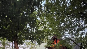 Una cabaña de troncos con porche y techo verde, rodeada de árboles.