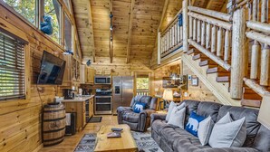 Interior acogedor de una cabaña con detalles de madera, un sofá, una mesita de centro y una escalera.