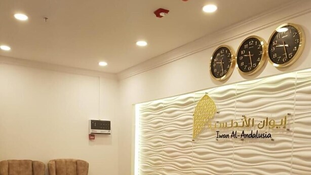 Un espace d’accueil comprenant trois fauteuils, une horloge murale et un mur décoratif orné d’un logo.