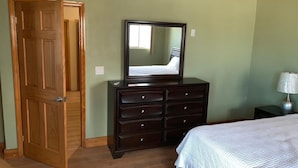 A bedroom with a wooden door, a dresser with drawers, a bed with a white bedspread, and a nightstand with a lamp. - Beautiful Bahamas Unit 4 (Nassau)