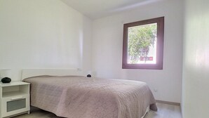 Een slaapkamer met een bed, een nachtkastje en een raam met uitzicht op bomen.