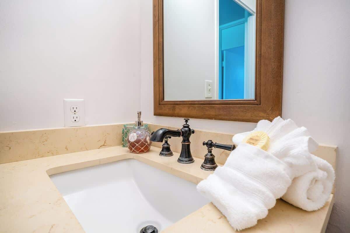 A bathroom with a sink, two faucets, a mirror, and a towel rack with towels.
