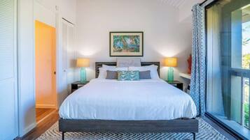 A bedroom with a bed, two bedside lamps, a framed picture above the bed, and a view through a window.