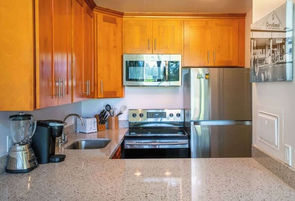 A kitchen with wooden cabinets, stainless steel appliances, a granite countertop, and a blender.