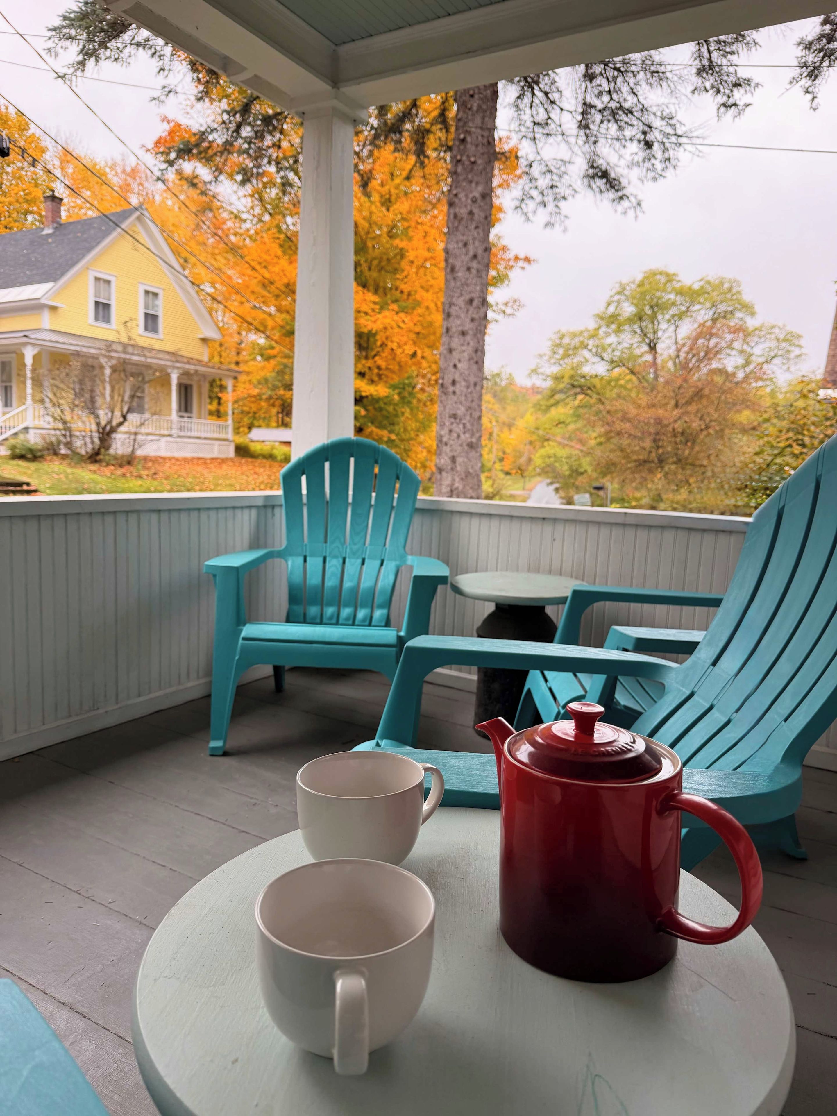 A porch with a table, two chairs, and a red pot.