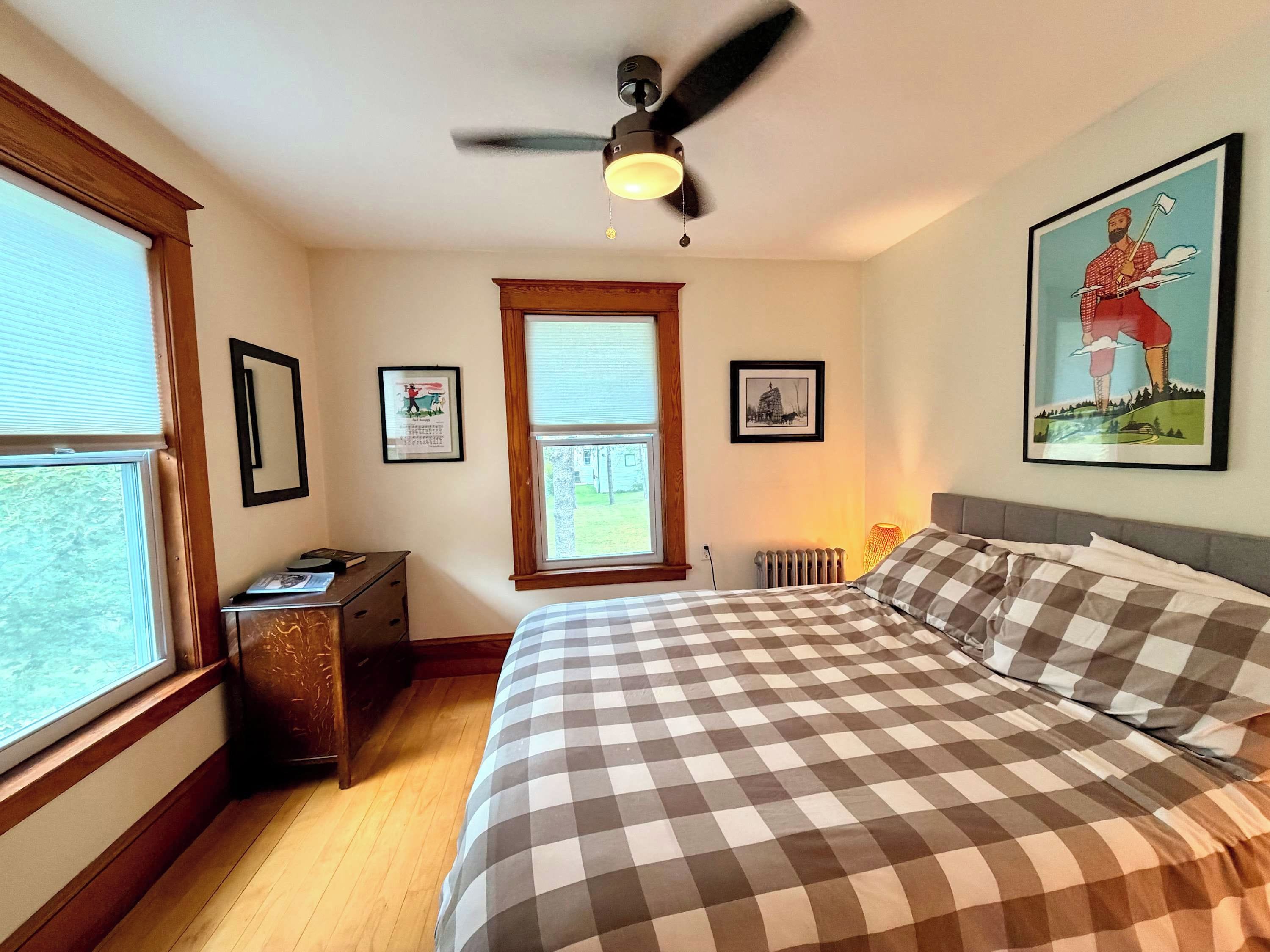A bedroom with a bed, a ceiling fan, a radiator, and framed pictures on the wall.