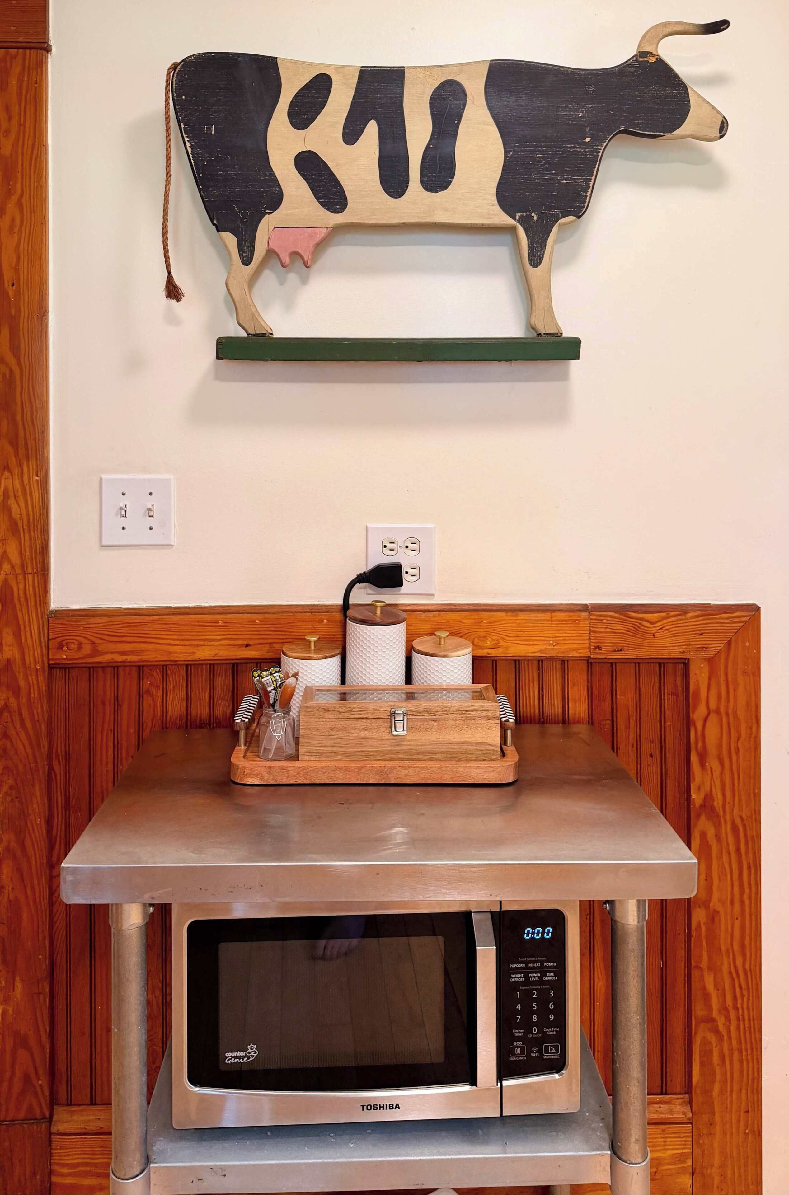 A kitchen with a microwave, a wooden counter, and a cow decoration on the wall.