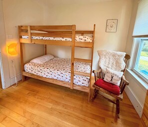 A bunk bed with a patterned bedspread, a chair with a red cushion, and a wall-mounted lamp. - Porch & Peak | 5BR Village Farmhouse in the White Mountains (Bethlehem)