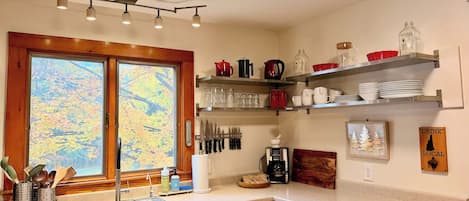 A kitchen with a window, wooden cabinets, a sink, and various kitchen items on shelves.