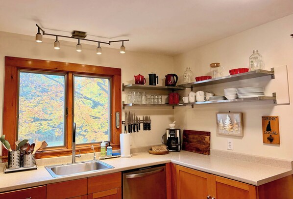 A kitchen with a window, wooden cabinets, a sink, and various kitchen items on shelves.
