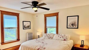 A bedroom with a bed, two bedside lamps, a ceiling fan, and two framed pictures on the wall.
