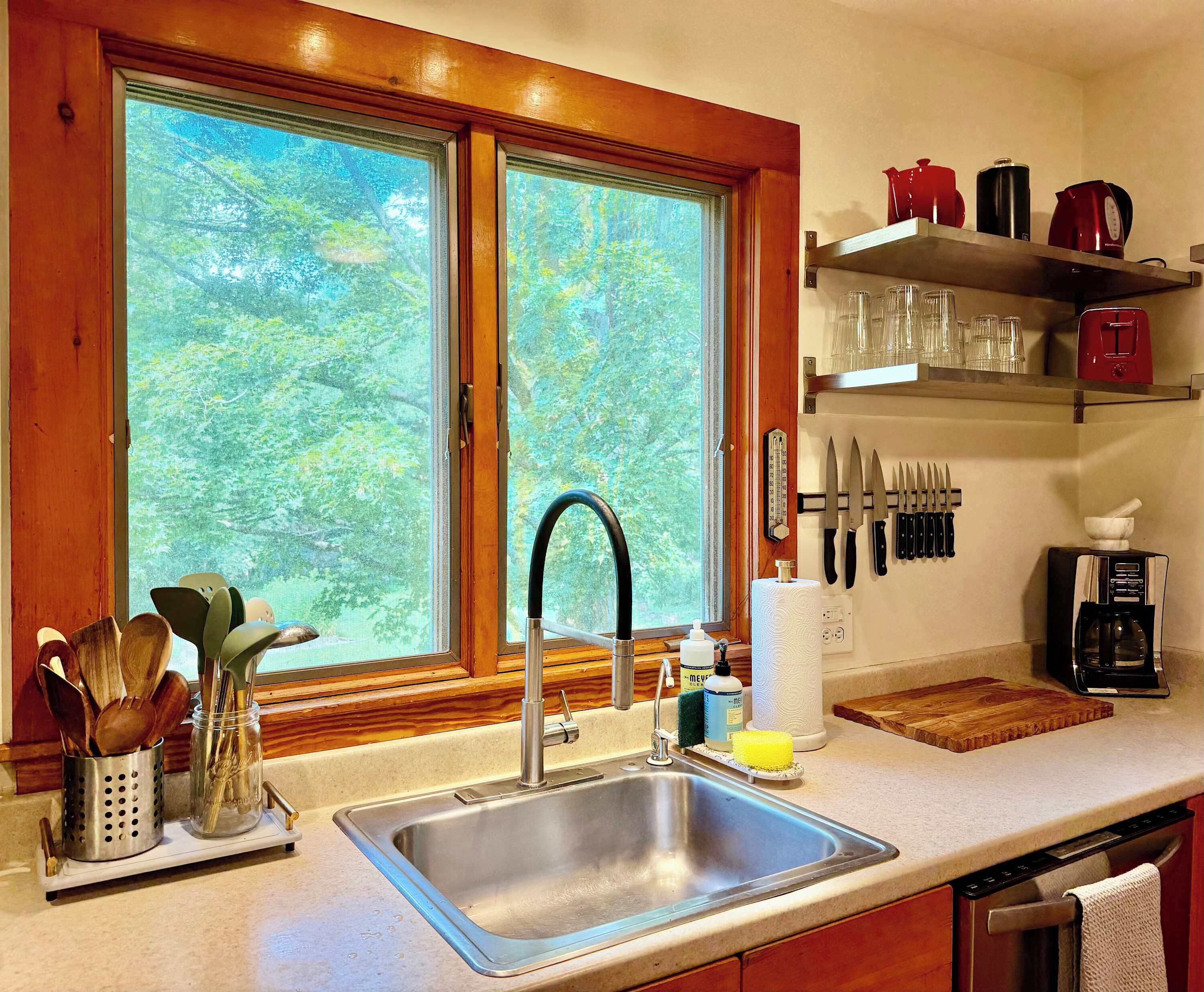 A kitchen with a stainless steel sink, wooden utensils, a coffee maker, and a knife block.
