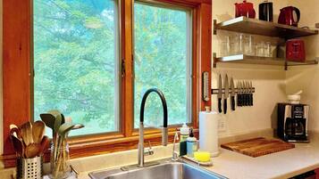 A kitchen with a stainless steel sink, wooden utensils, a coffee maker, and a knife block.