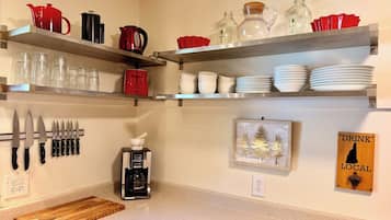 Une cuisine avec des étagères où sont rangés divers ustensiles, une machine à café et une planche à découper en bois.