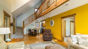 A spacious living area with a wooden staircase, a dining table with chairs, a large armchair, and a sofa. - Blue Spruce . Trailside Lodging (Millersburg)