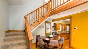 A staircase with wooden railings leading to a dining area with a round table and bar stools. - Blue Spruce . Trailside Lodging (Millersburg)