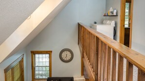 Un loft espacioso con techo alto, una escalera de madera, un sofá modular negro, una mesa de centro redonda y un ventanal grande.