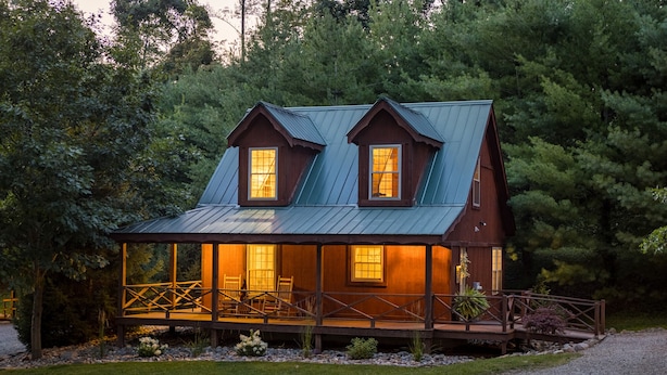 A wooden cabin with a metal roof, a covered porch, and a gravel driveway.