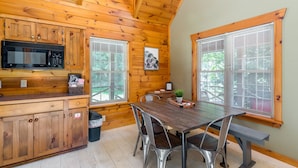A wooden cabin interior with a kitchen, dining area, and large windows.