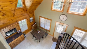 A loft-style room with a wooden ceiling, a dining table, a clock, and large windows.