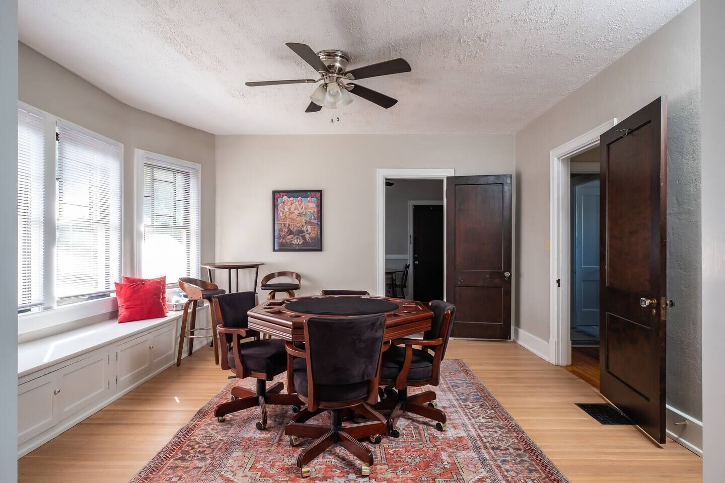 Un coin repas comprenant une table ronde, des chaises, un ventilateur de plafond et une fenêtre avec des stores.