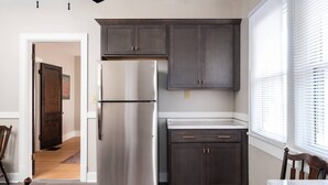 Une cuisine moderne avec des meubles de couleur sombre, un réfrigérateur en acier inoxydable et une fenêtre équipée de stores.