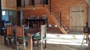 A wooden cabin interior with a dining area, staircase, and a large wooden door.