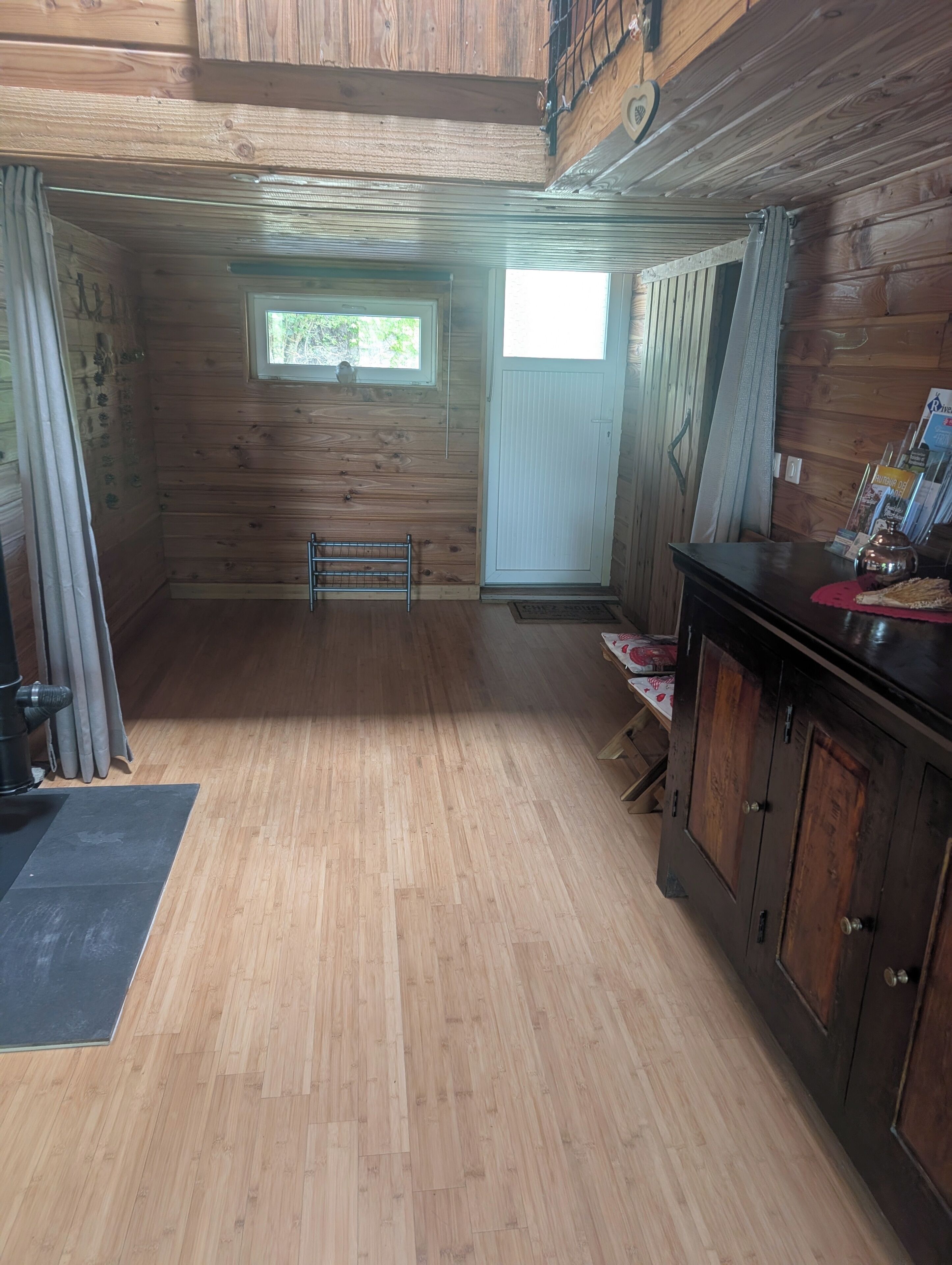 Un intérieur en bois, avec un plancher en bois, une fenêtre, une porte et une petite table sur laquelle se trouve une bouilloire.