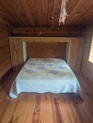 Una habitación de cabaña de madera con una cama, paredes de madera y techo inclinado.
