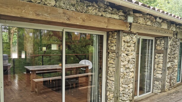 A wooden deck with a stone wall, large sliding glass doors, and a bench.