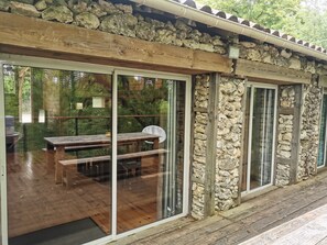 Terraza de madera con un muro de piedra, puertas correderas de vidrio y un banco.