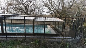 A swimming pool with a glass enclosure, surrounded by a metal fence and trees.