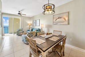 A dining area with a wooden table and wicker chairs, a blue sofa, and a ceiling fan.