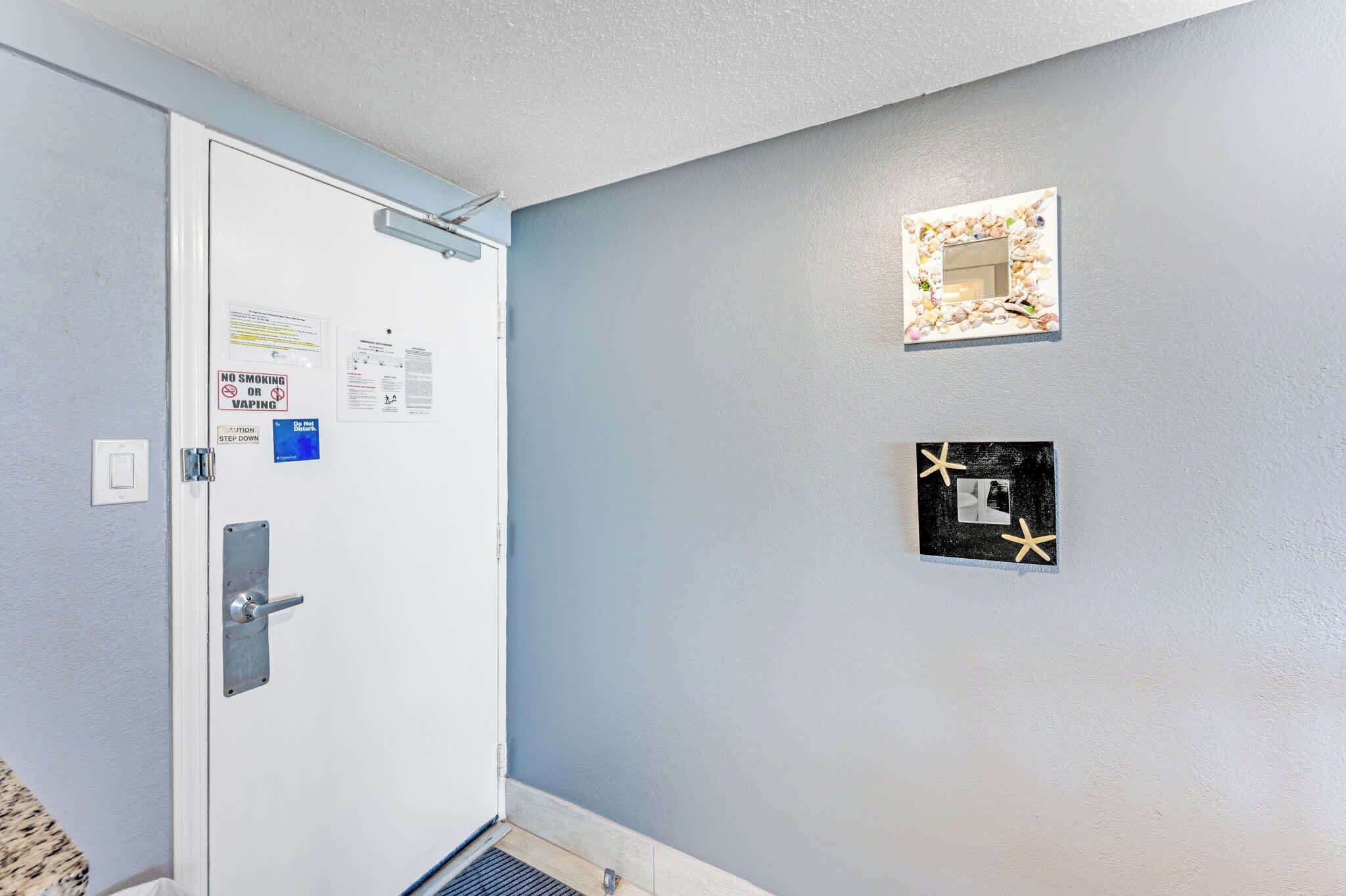 Un couloir avec une porte blanche, un luminaire fixé au mur et une grille d’aération.