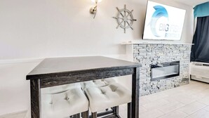 Un coin repas avec une table et des chaises, un téléviseur fixé au mur, un élément de décoration représentant un gouvernail de bateau et une cheminée.