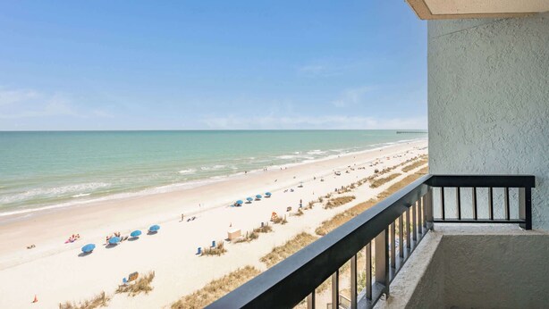 Un balcon donnant sur une plage, avec une balustrade et un ciel dégagé.