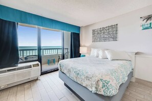 Hotelkamer met een bed, uitzicht op zee, een balkon met een stoel en een kunstwerk aan de muur.