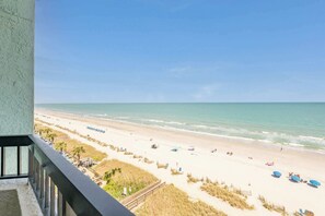 A beach view from a balcony with a clear sky, sandy beach, and umbrellas.