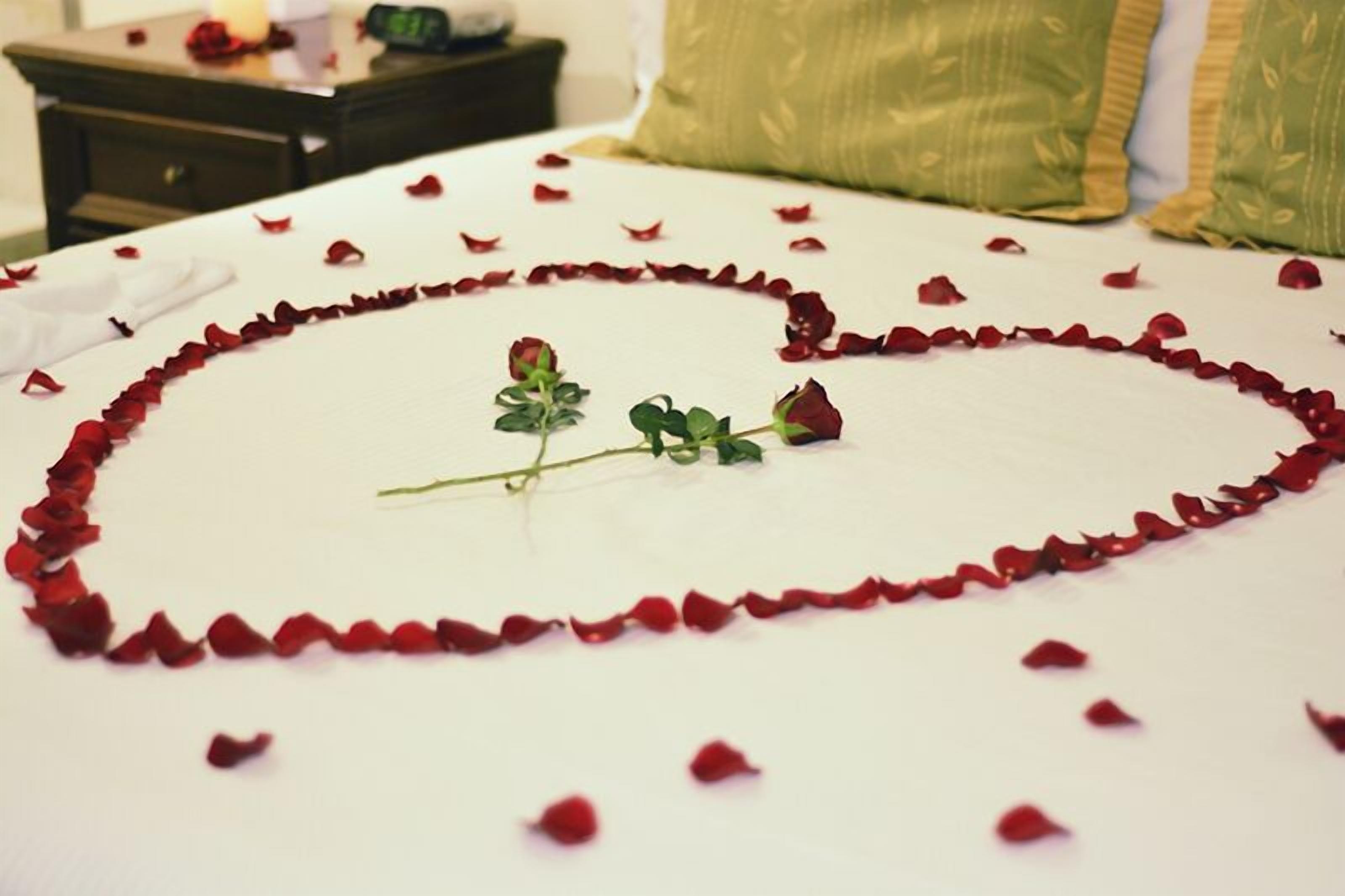 Un lit recouvert de pétales de rose disposés en forme de cœur, avec une seule rose posée dessus.