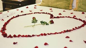 Un lit recouvert de pétales de rose disposés en forme de cœur, avec une seule rose posée dessus.