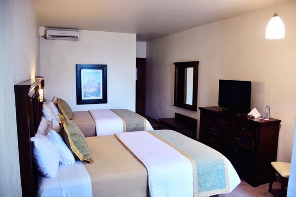 A hotel room with two beds, a television, a dresser, and an air conditioning unit.