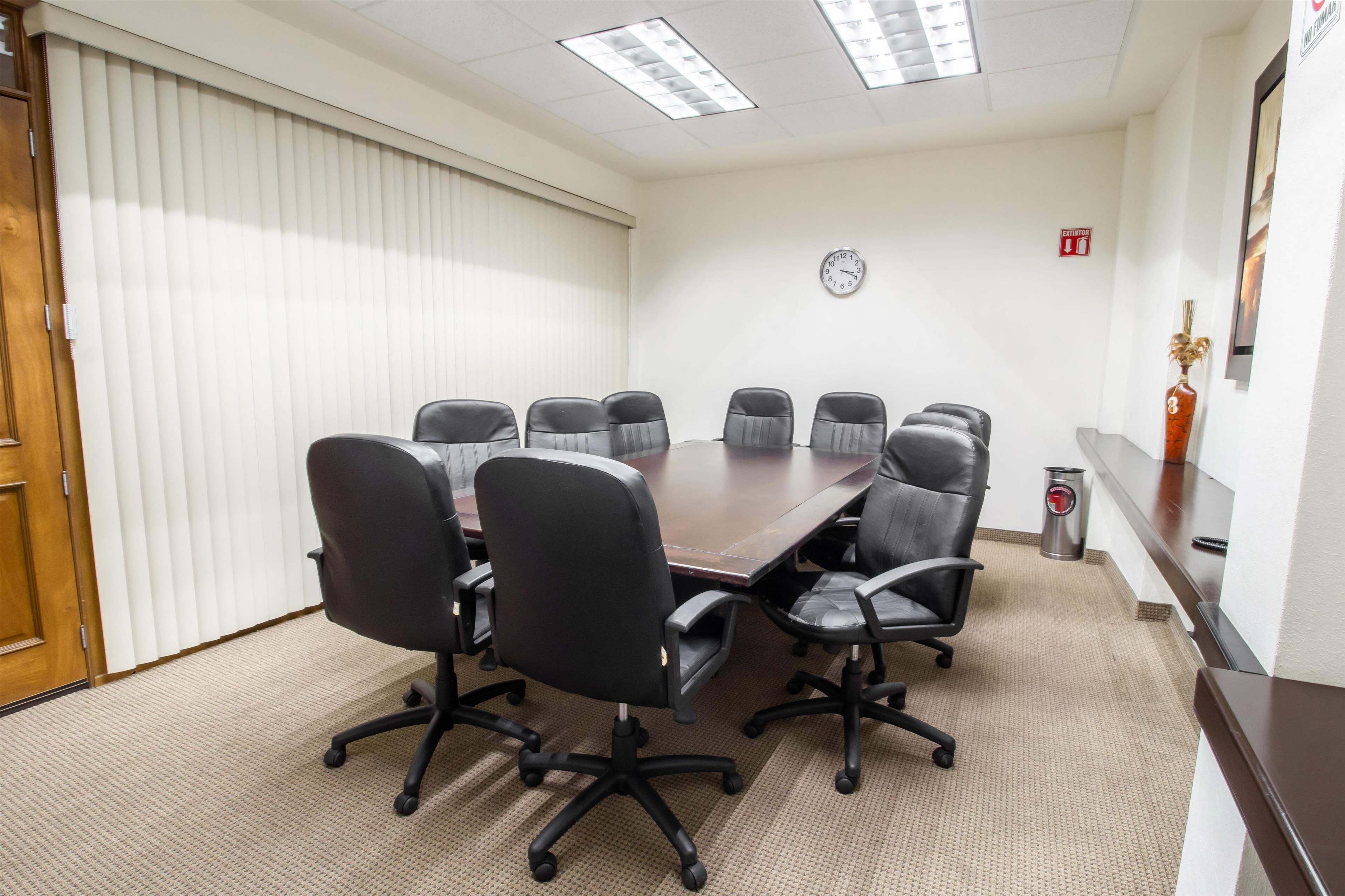 A conference room with a large table, eight chairs, a clock on the wall, and a fire extinguisher.